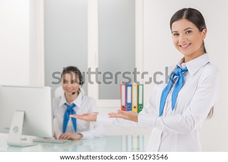 Customer service representative at work. Cheerful young female customer service representative pointing her coworker working at the computer and smiling