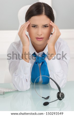 Tired customer service representative. Depressed young female customer service representative sitting at her working place and holding her head in hands
