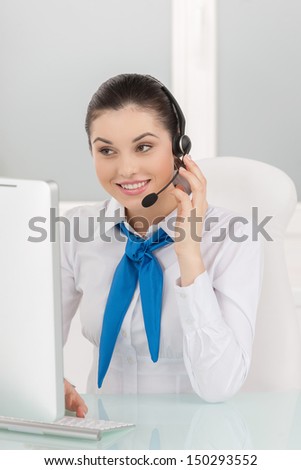 Customer service representative at work. Cheerful young female customer service representative in headset working at the computer