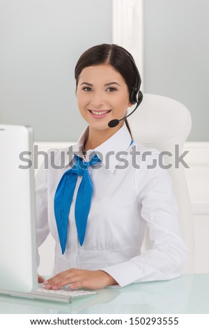 Young customer service representative. Cheerful young female customer service representative in headset working at the computer and smiling at camera