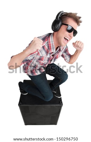 Turn the volume up. Cheerful young man in sunglasses listening to the music while sitting on the speaker