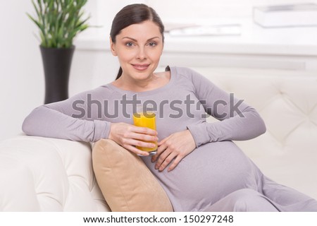 Pregnant woman with juice. Smiling pregnant woman sitting on the couch and holding a glass of orange juice