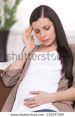 Headache. Mature pregnant woman holding her hand on head and expressing negativity