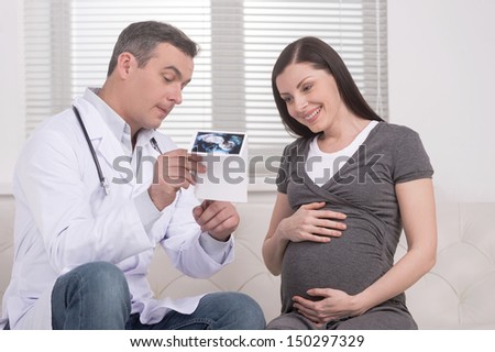 Doctor and pregnant woman. Confident mature doctor showing the ultrasound photographs to pregnant woman