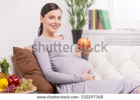 Pregnant woman with apple. Smiling pregnant woman lying on couch and holding apple