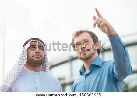 Discussing business issues. Low angle view of two business partners discussing something while one of them pointing away and smiling