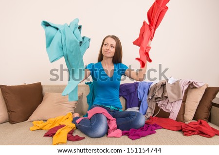 What a mess! Woman choosing clothes to wear while sitting on the couch