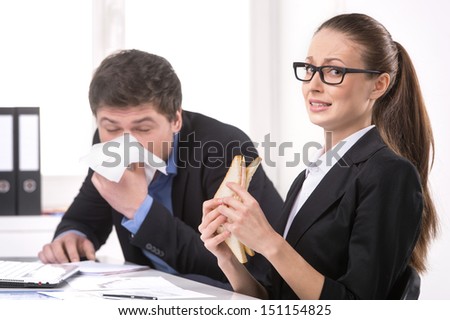 Man sneezing. Businessman sneezing while woman eating sandwich near him