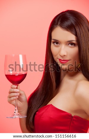 Woman with glass of wine. Beautiful young woman in red dress holding a glass with wine and looking at camera