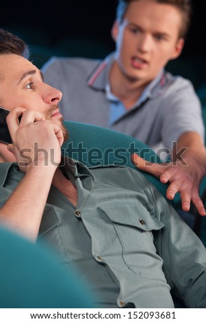 Stop talking! Young men talking at phone while watching movie at cinema
