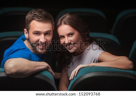 Couple at cinema. Young couple looking over shoulder while sitting at cinema