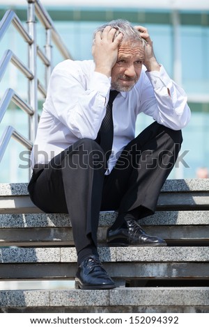Depressed businessman. Depressed senior man in formalwear holding his head in hands while sitting on stairs