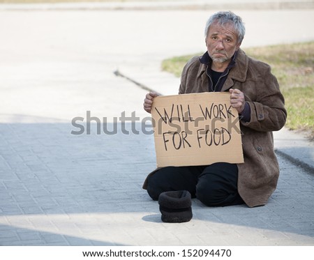 Will work for food. Depressed man in dirty wear sitting on the floor outdoors and holding poster
