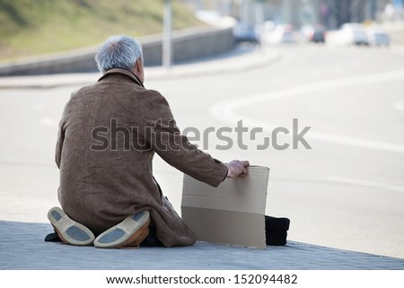 Tramp. Rear view of depressed man sitting on his knees and holding poster