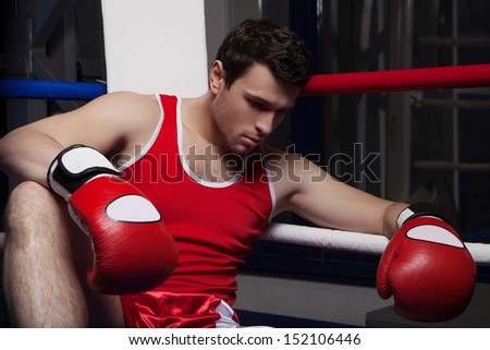 Defeated boxer. Disappointed young boxer sitting on the boxing ring and looking down