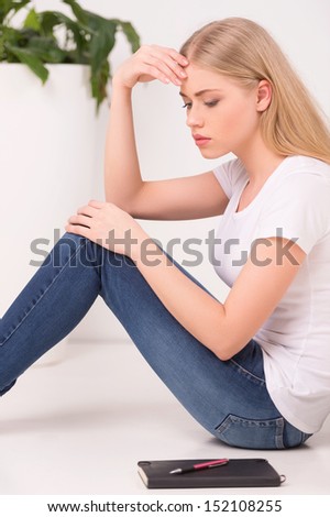 Thoughtful woman. Side view of beautiful young blond hair woman sitting on the floor and holding head in hand