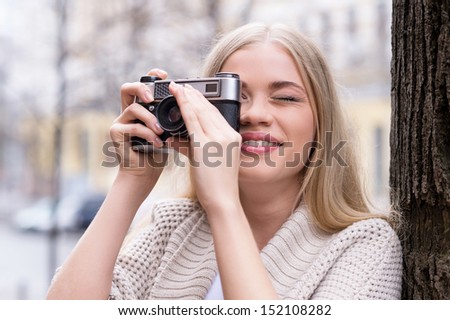 Woman photographing. Beautiful young blond hair woman holding camera and taking photos while standing outdoors