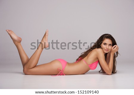 Beauty In Pink Bikini. Attractive Young Woman In Bikini Lying Front And Looking At Camera While Isolated On Grey