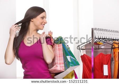 Retail store. Cheerful young woman with shopping bags looking at the dresses in retail store