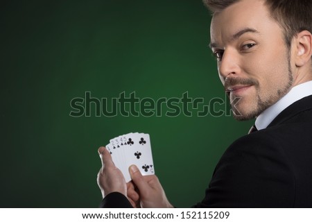 Man with cards. Cheerful young man in formalwear holding cards in his hands and looking over shoulder while isolated on green