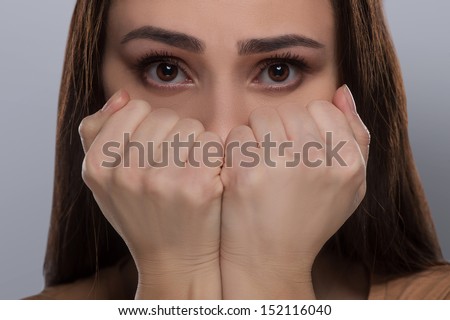 Scared woman. Terrified young woman covering mouth with hands and looking at camera while isolated on grey