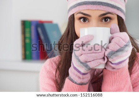 Cold and flue. Beautiful young woman in hat and gloves drinking tea while sitting at home