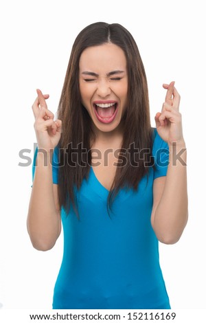 Fingers crossed. Happy young woman with closed eyes holding her fingers crossed while standing isolated on white