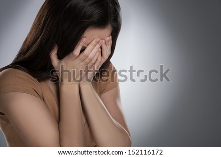 Depressed woman. Sad young woman covering face with hands while isolated on grey