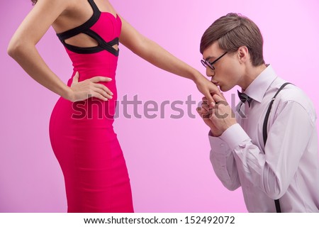 Nerd and beauty. Side view of young nerd man kissing woman hand while standing together against pink background