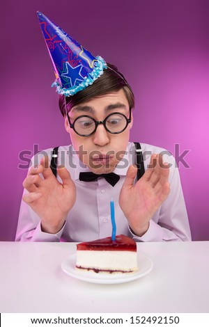 Nerds birthday. Young cheerful nerd man in glasses sitting at the table with a birthday cake on it