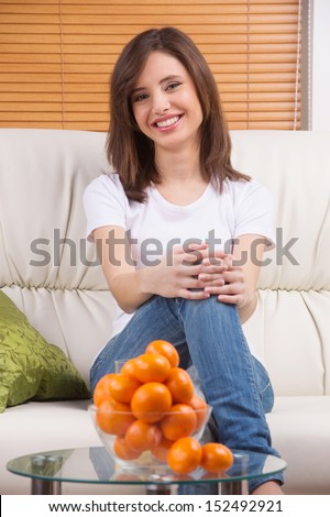 Woman and oranges. Cheerful young woman sitting on the coach and looking at camera