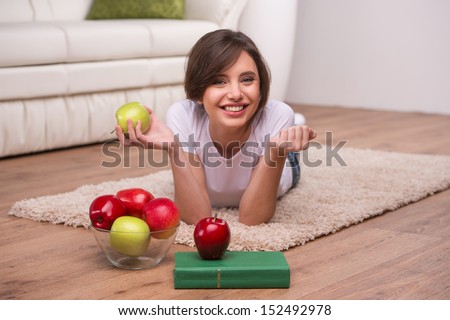 Woman relaxing at home. Beautiful young woman lying on the floor at home and holding apples