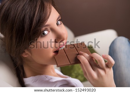 Woman eating chocolate. Beautiful young woman sitting on the coach and eating chocolate