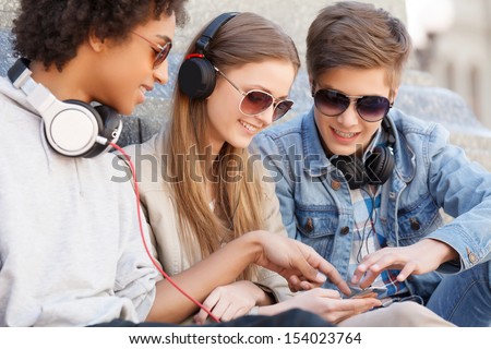 Teenage Friends. Three Cheerful Teenage Friends Sitting Close To Each Other And Listening To The Music
