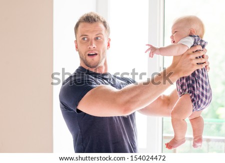 Man with baby. Frustrated young man holding baby in his hands and looking away