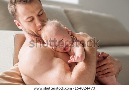Man with baby. Young muscular man holding a crying baby in his hands