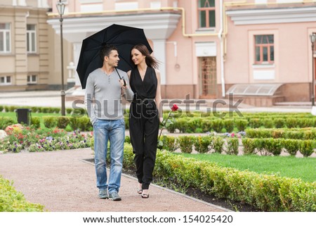 Loving couple with umbrella. Cheerful young couple walking on street while man holding umbrella