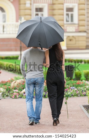 Loving couple with umbrella. Rear view of young couple walking on street while man holding umbrella