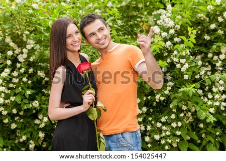 Beautiful couple. Cheerful young couple standing close to each other while man pointing away and smiling