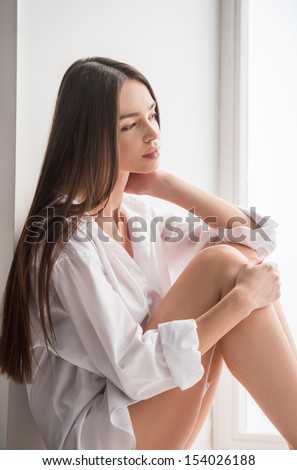 Beauty on the window sill. Beautiful young woman sitting on the window sill and looking through the window