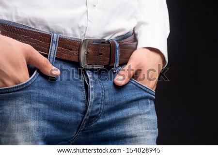 Man in jeans. Close-up of man holding hands in jeans pockets while standing against black background