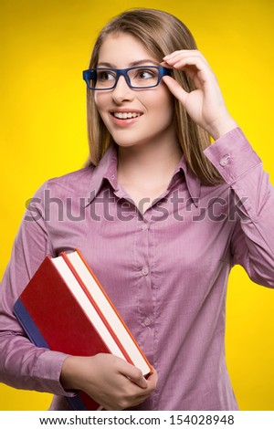 Intelligence female student. Smiling young women holding books in her hand while standing against yellow background