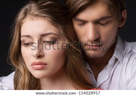 Depressed couple. Depressed young couple standing close to each other while isolated on black