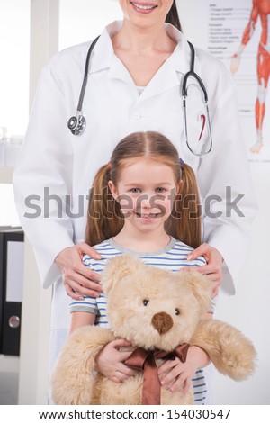 Doctor and little patient. Cropped image of cheerful doctor standing close to little girl with toy bear