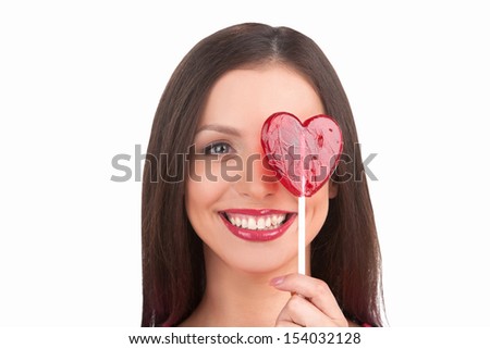 Girl with lollipop. Portrait of beautiful young woman holding heart shape lollipop in front of her eye while isolated on white