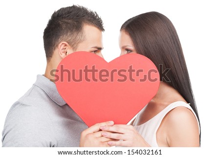 Loving couple. Beautiful young loving couple standing face to face and holding big paper heart while isolated on white