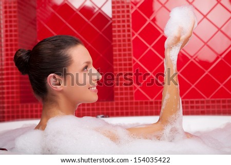 Cheerful beauty in bath. Side view of beautiful young woman lying in bathtub and smiling