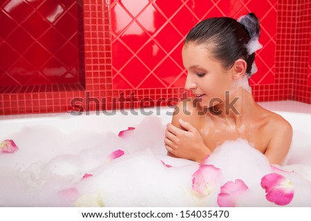 Beauty in bath.  Attractive young woman lying in bubble bath full of flower petals and smiling