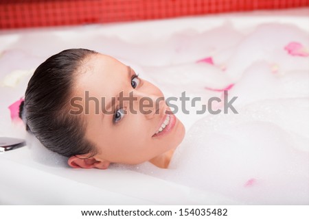 Beauty in bath.  Top view of attractive young woman lying in bubble bath full of flower petals and smiling
