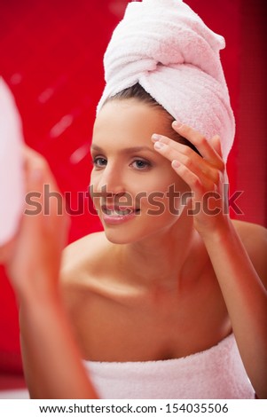 Looking at the mirror. Beautiful young woman covered with towel looking at herself at the mirror and smiling